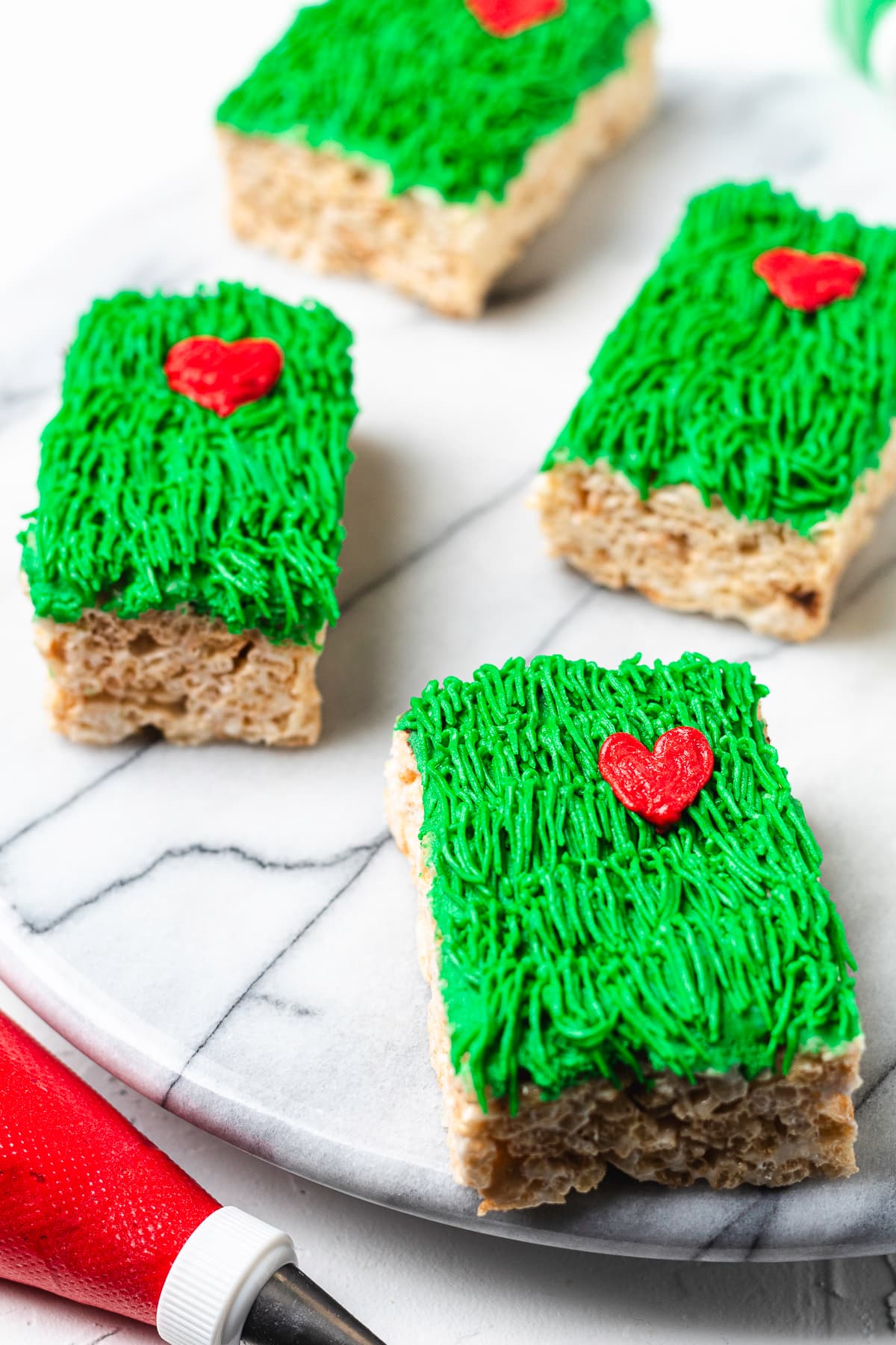 Grinch Rice Krispie treats decorated with green frosting and red hearts.