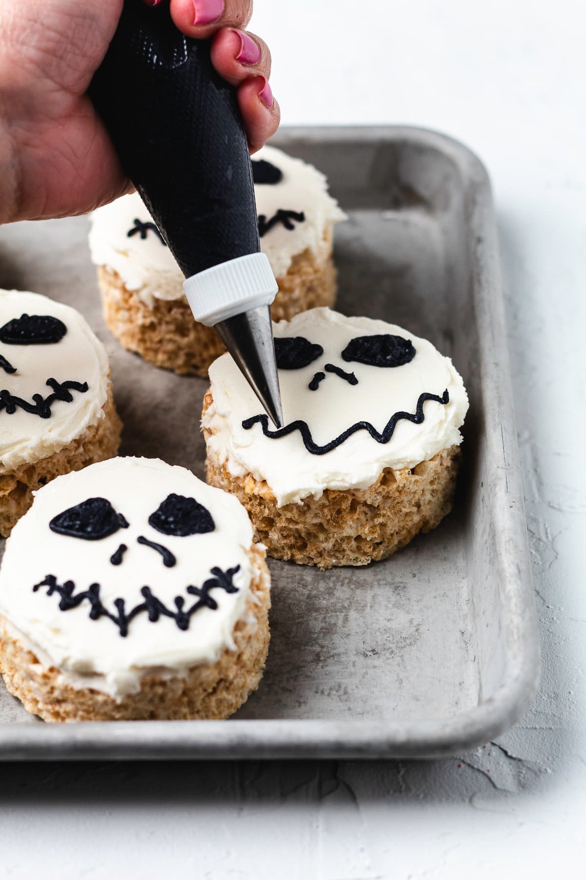 Piping black frosting onto Jack Skellington Rice Krispie treats.