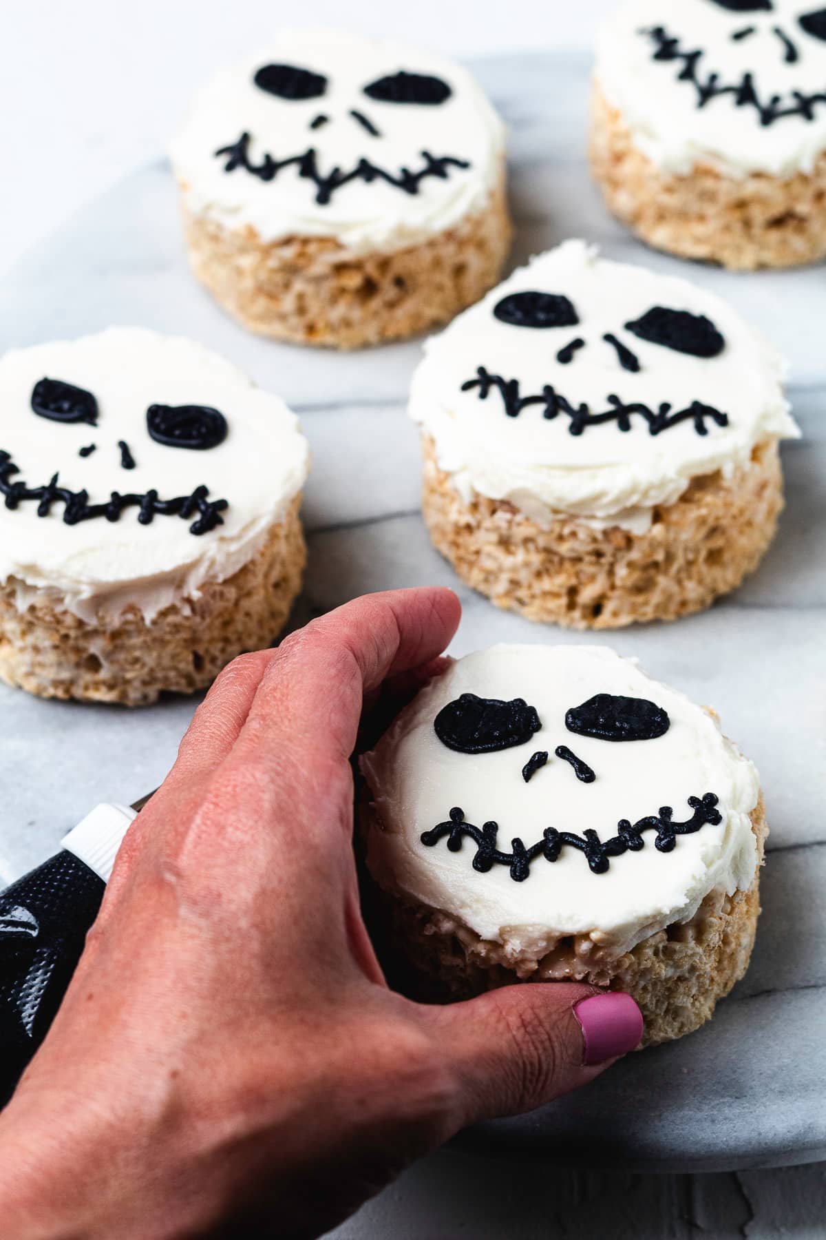 Hand holding a Jack Skellington Rice Krispie treat with frosting face.