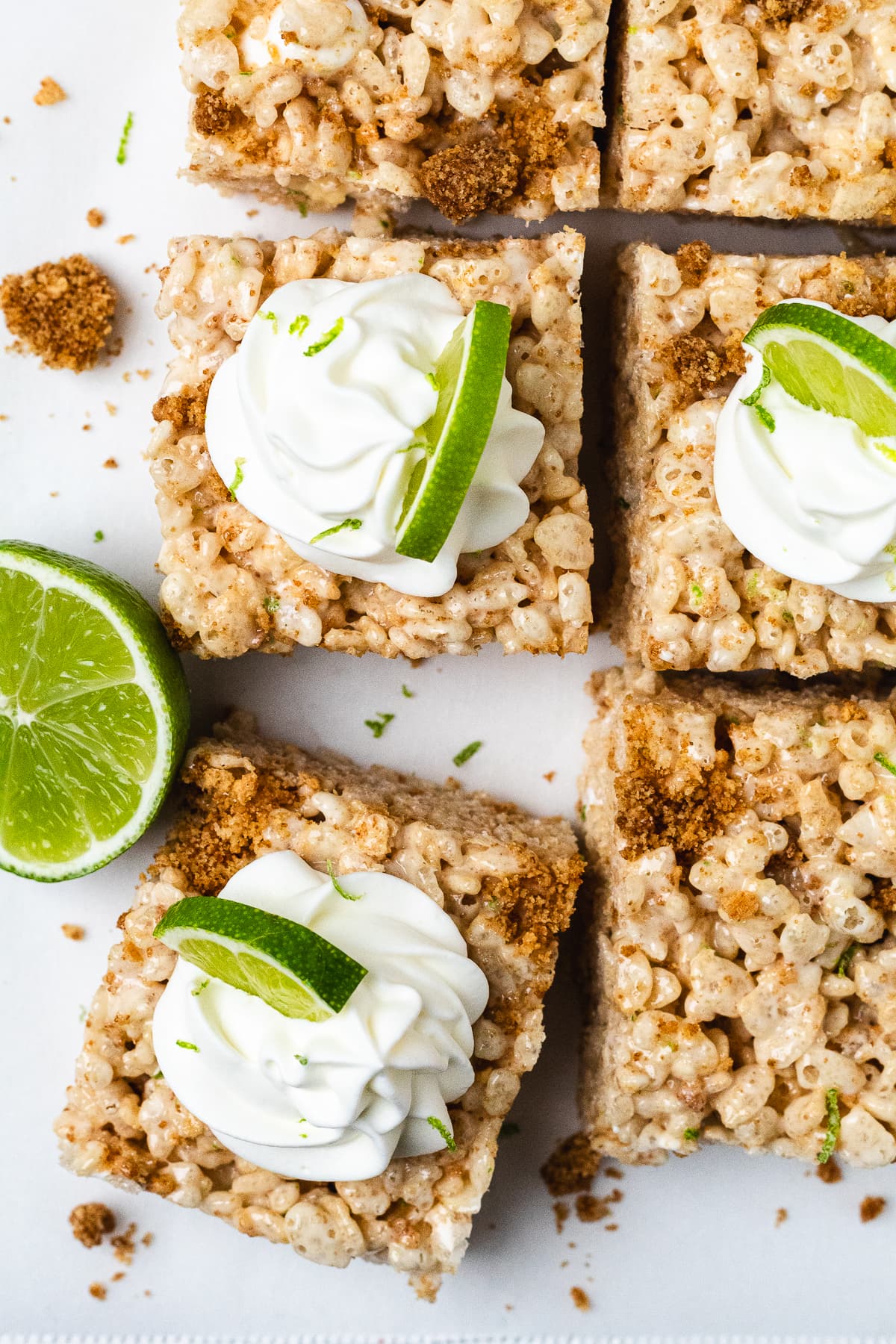 Overhead view of key lime Rice Krispie treats topped with whipped cream, lime slices, and graham cracker crumbs.