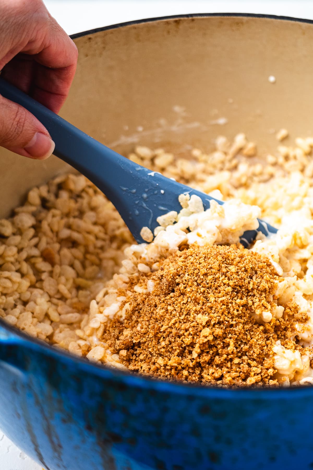 Adding graham cracker crumbs to key lime Rice Krispie treat mixture in a Dutch oven.