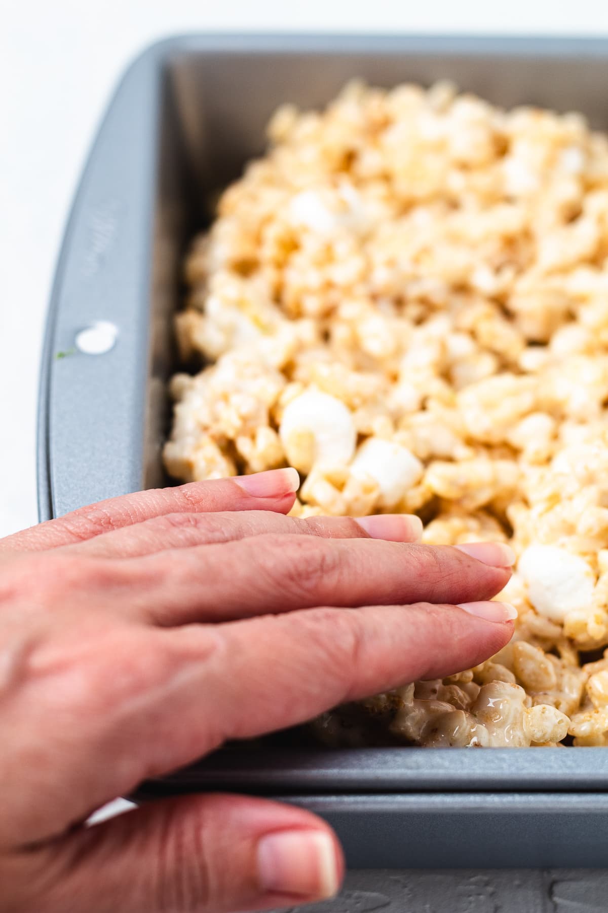 Pressing key lime Rice Krispie treat mixture into a baking pan by hand.