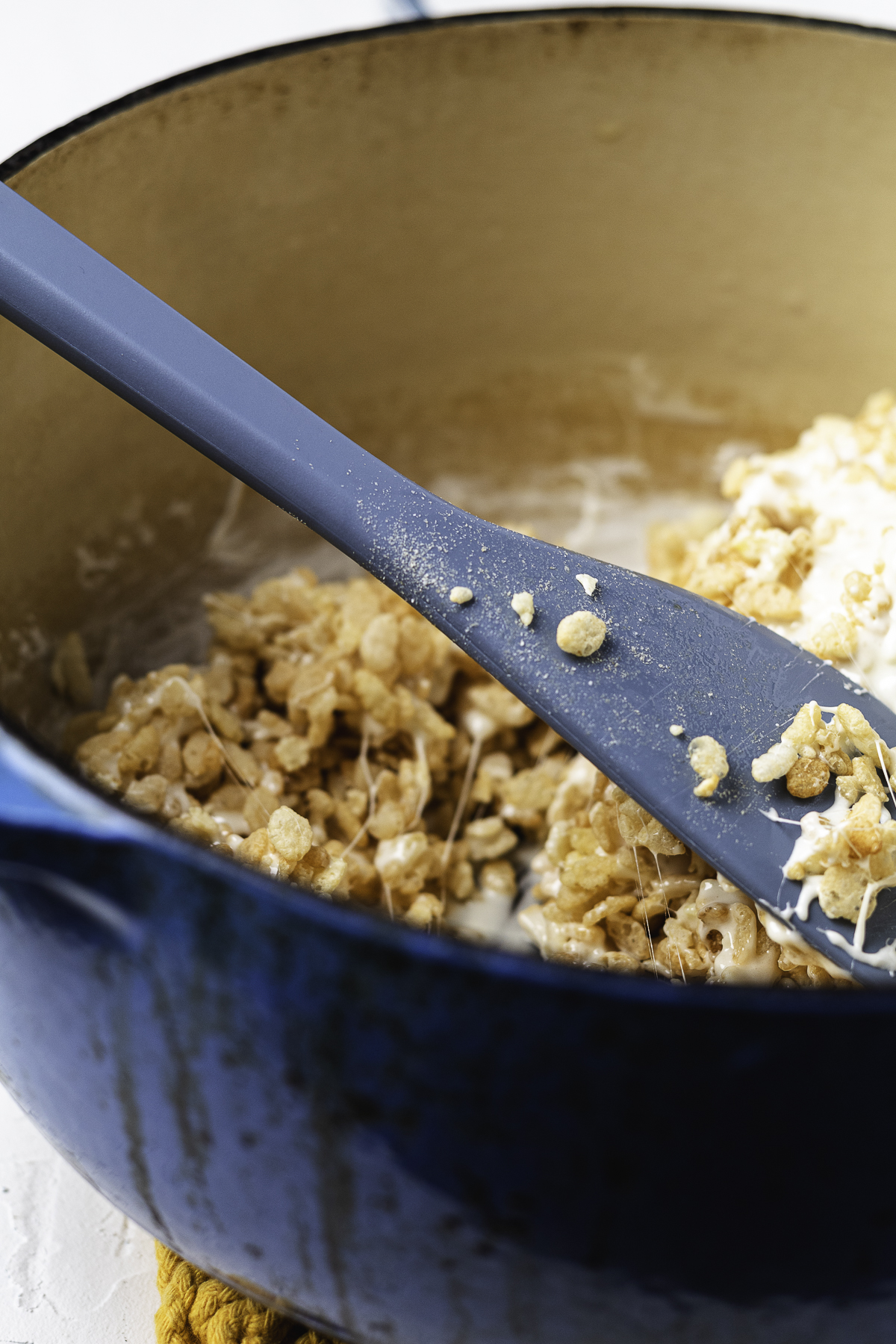 Mixing cereal Rice Krispie treats mixture in a blue Dutch oven.