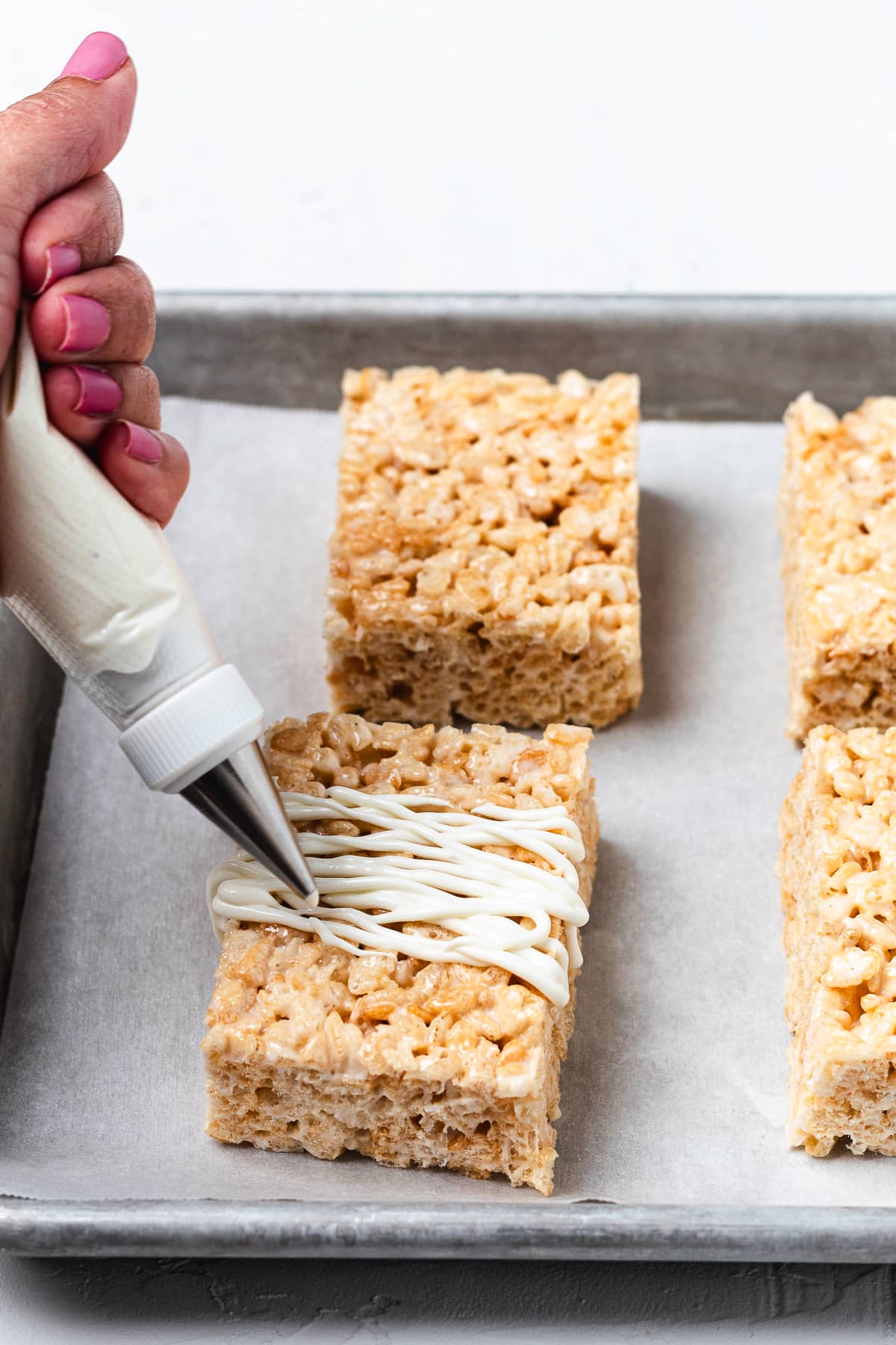 Hand piping white candy melts onto Rice Krispie treat.