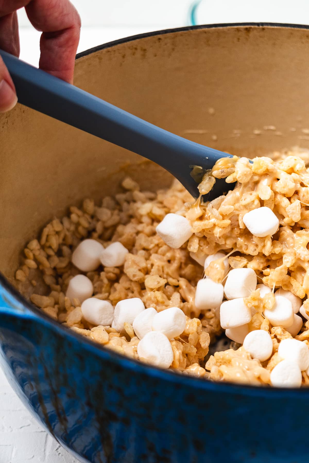 Folding mini marshmallows into the cereal mixture.