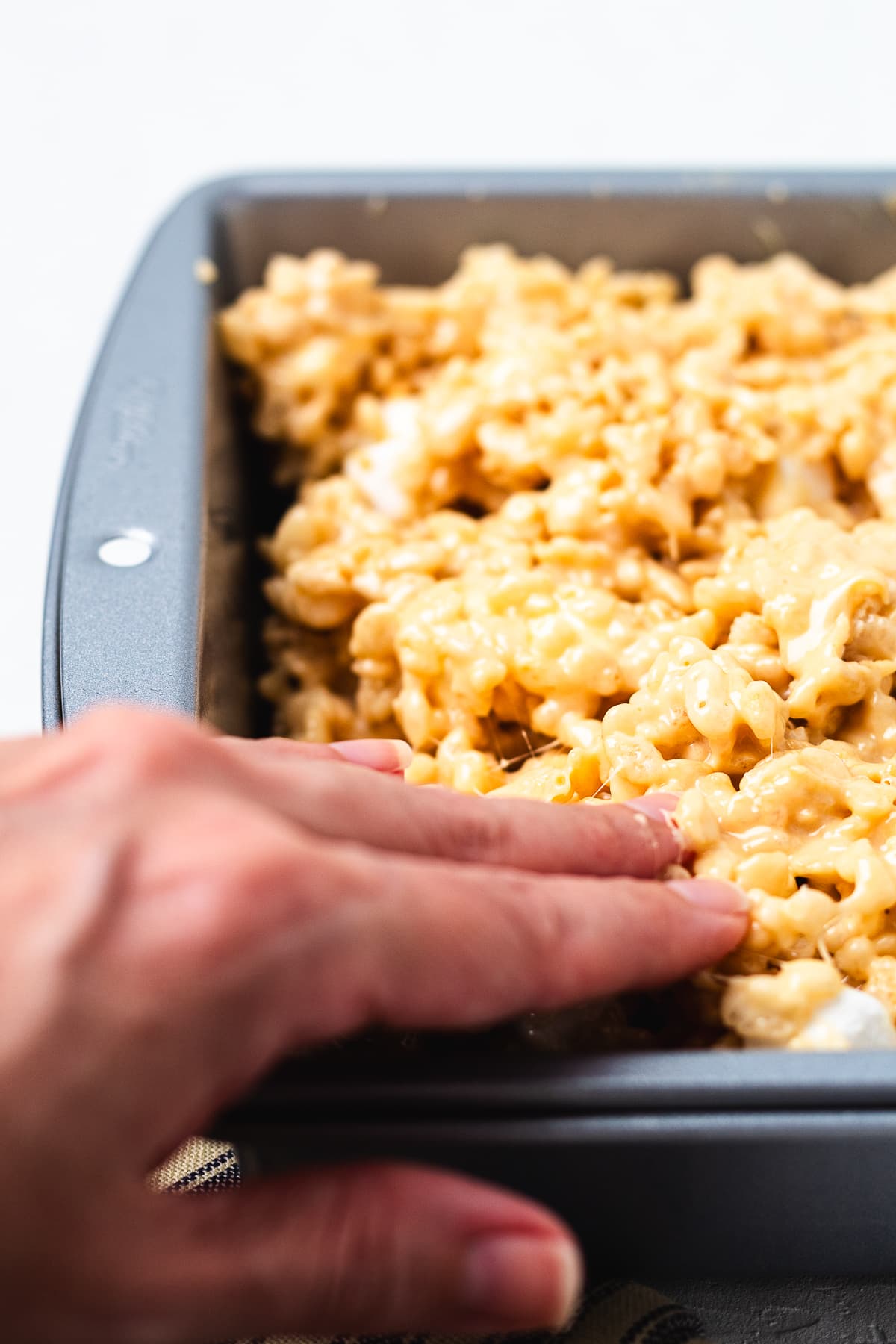 Pressing salted caramel Rice Krispie treats into a 9x13 pan.