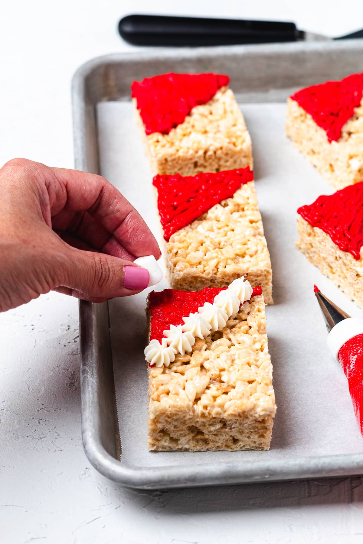 Adding a mini marshmallow pom-pom to a Santa hat Rice Krispie treat.