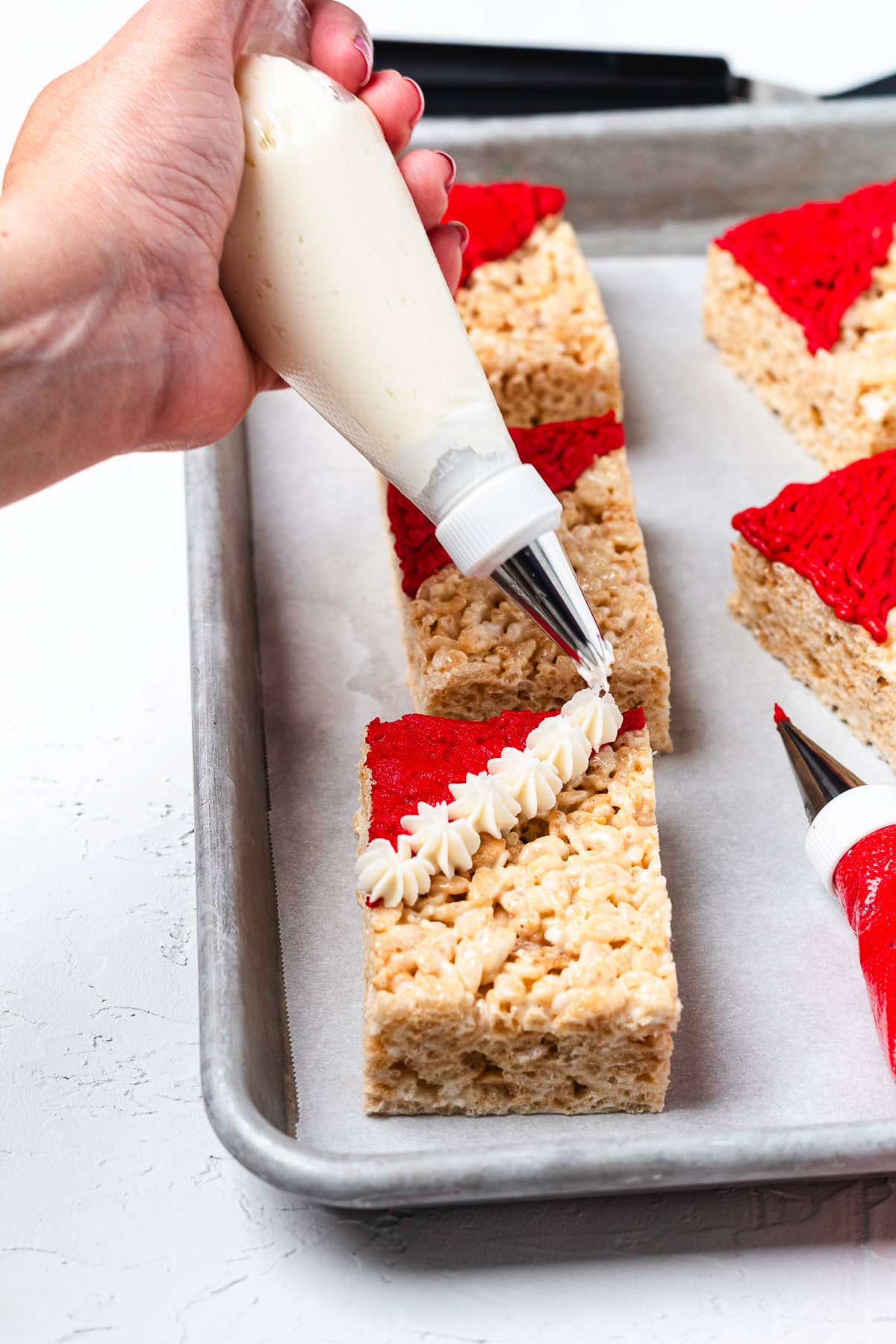 Piping white frosting trim onto a Santa hat Rice Krispie treat.