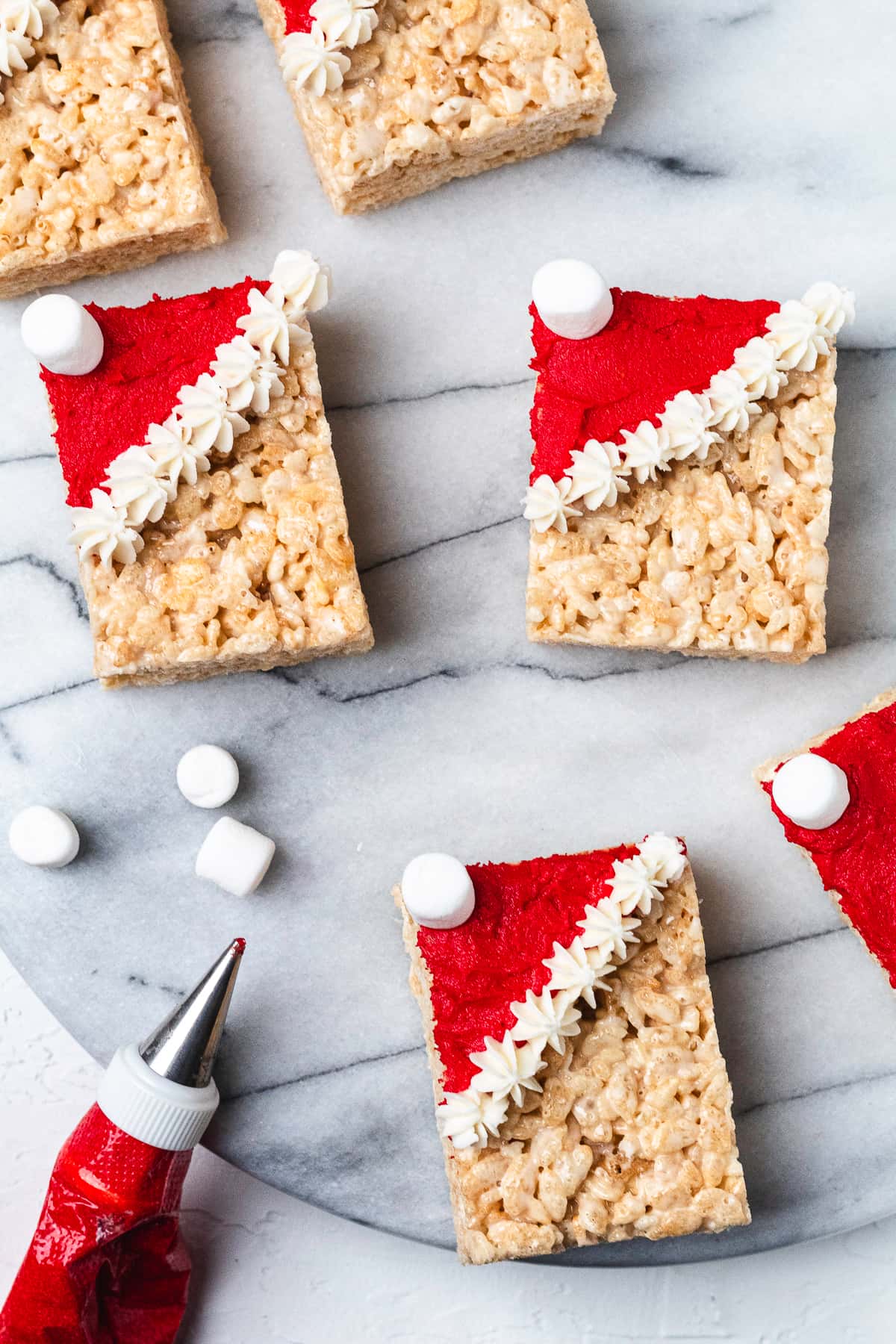 Santa hat Rice Krispie treats decorated with red frosting and mini marshmallows.