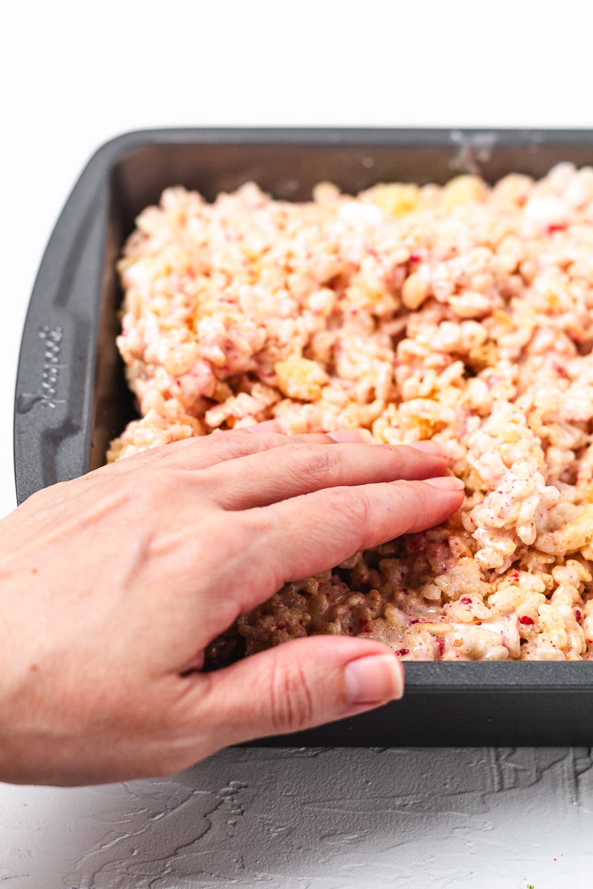 Pressing strawberry shortcake Rice Krispie treats into a baking pan by hand.