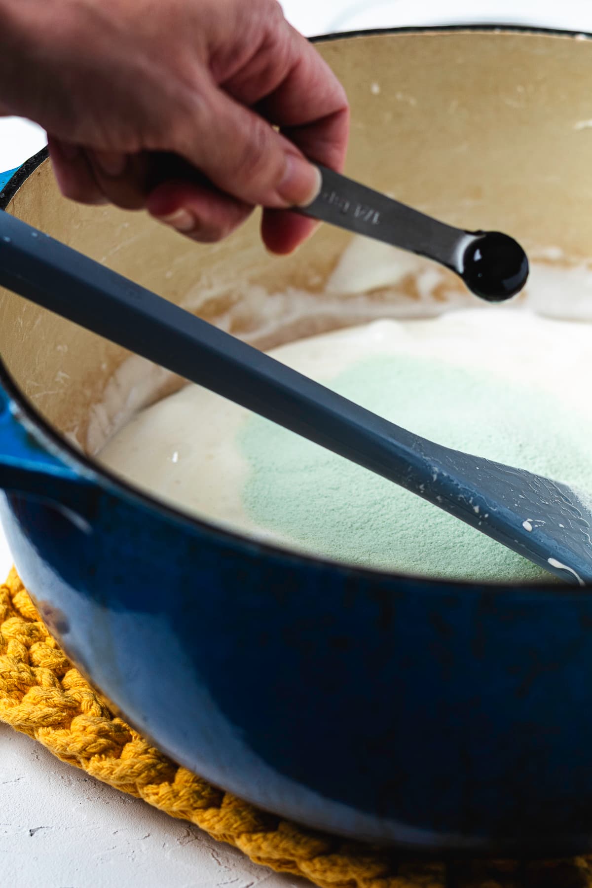 Adding green food coloring to the melted marshmallow mixture.
