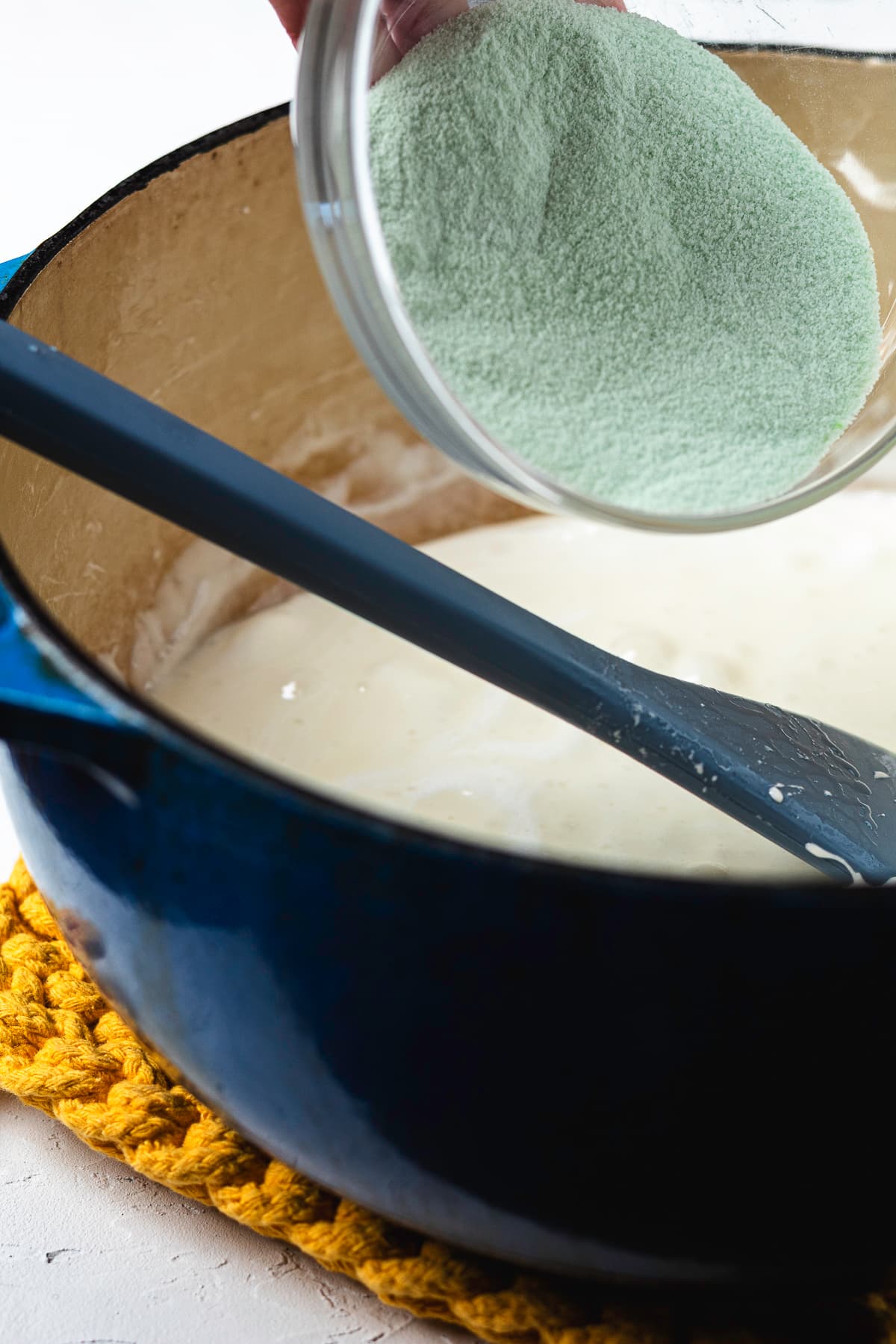 Pouring green apple gelatin mix into the melted marshmallow mixture.