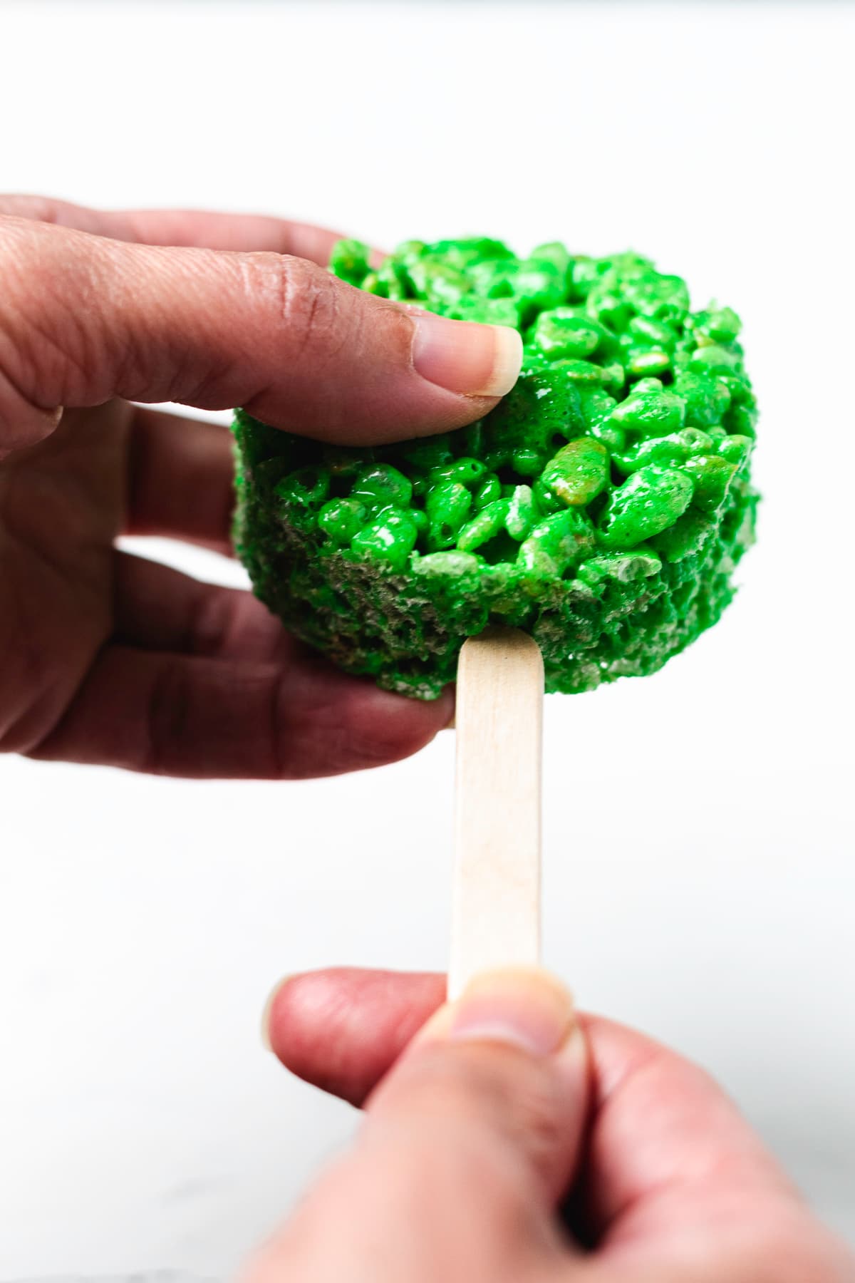 Inserting a wooden stick into a round green Rice Krispie treat.
