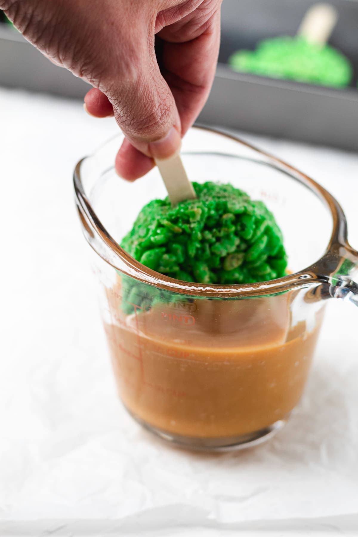 Dipping a green Rice Krispie treat pop into melted caramel.
