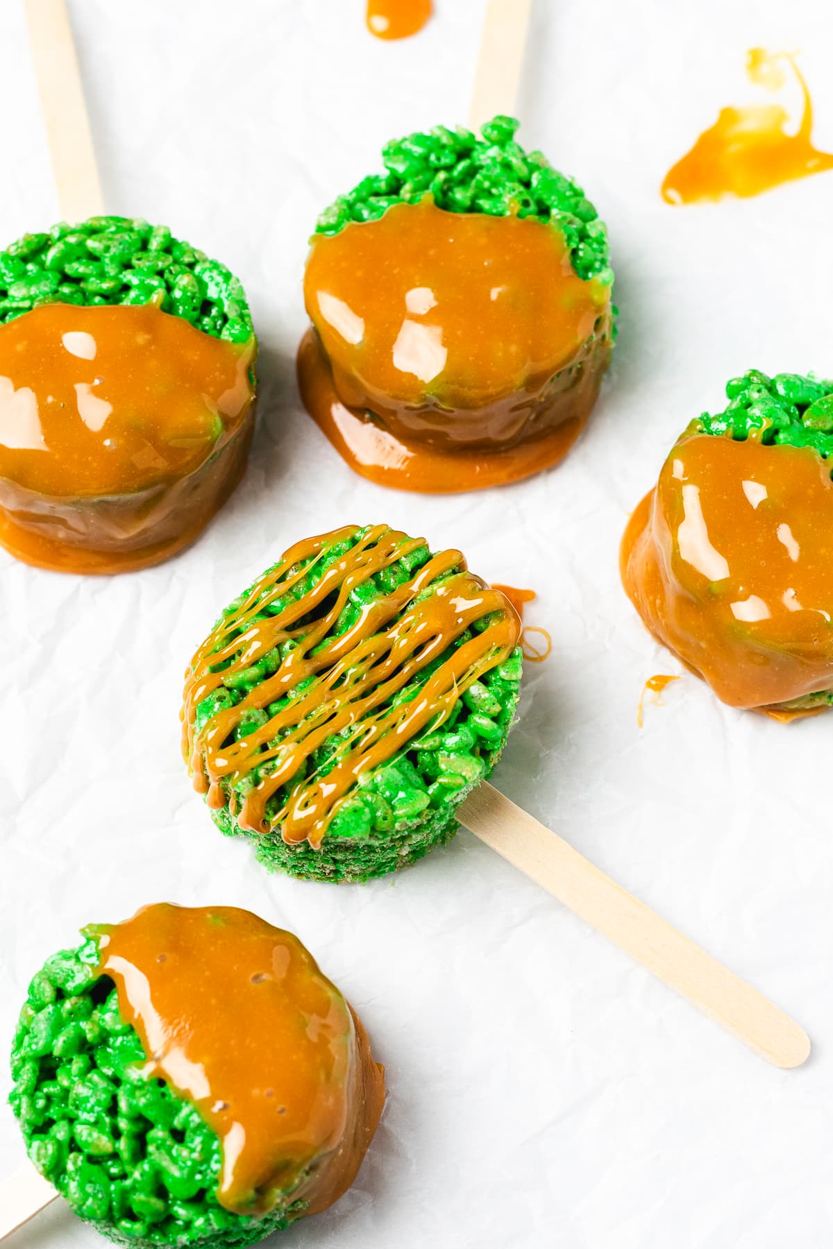 Green caramel apple Rice Krispie treat pops arranged on parchment paper.