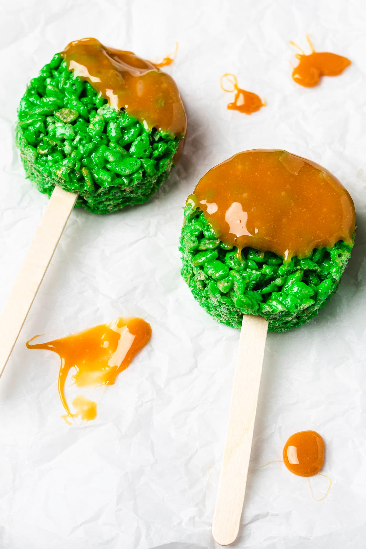 Two caramel apple Rice Krispie treat pops on parchment paper.
