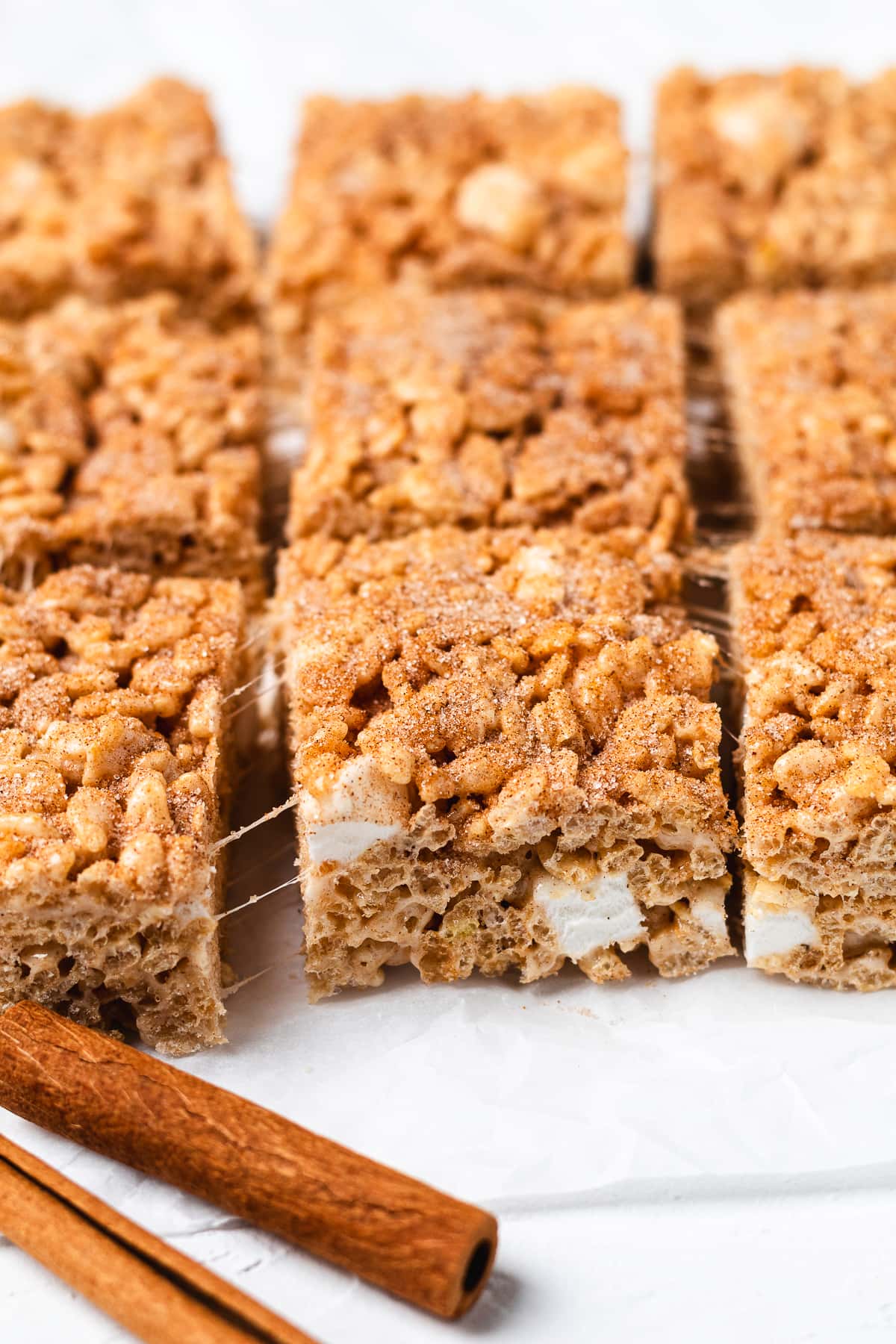 Snickerdoodle Rice Krispie Treats topped with cinnamon sugar and served with cinnamon sticks.