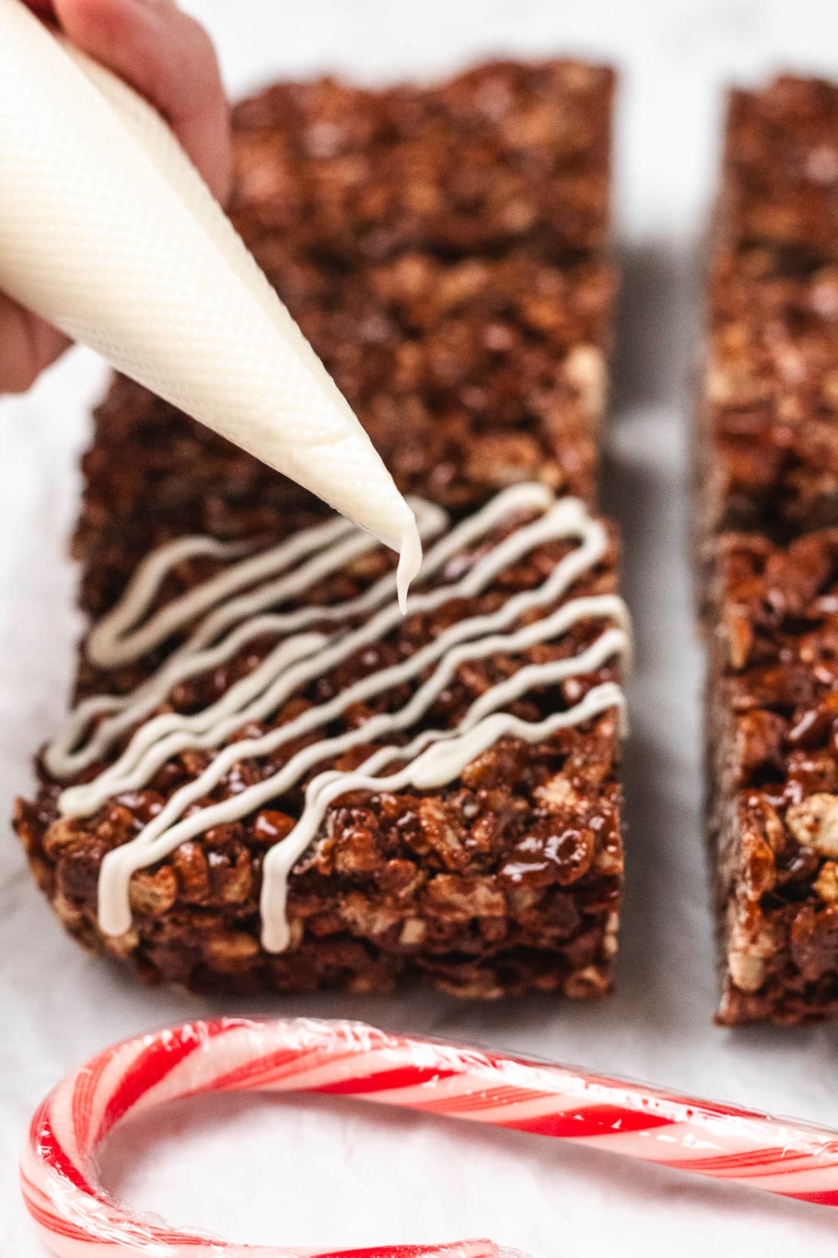 White chocolate being drizzled over chocolate Rice Krispie treats with a piping bag.