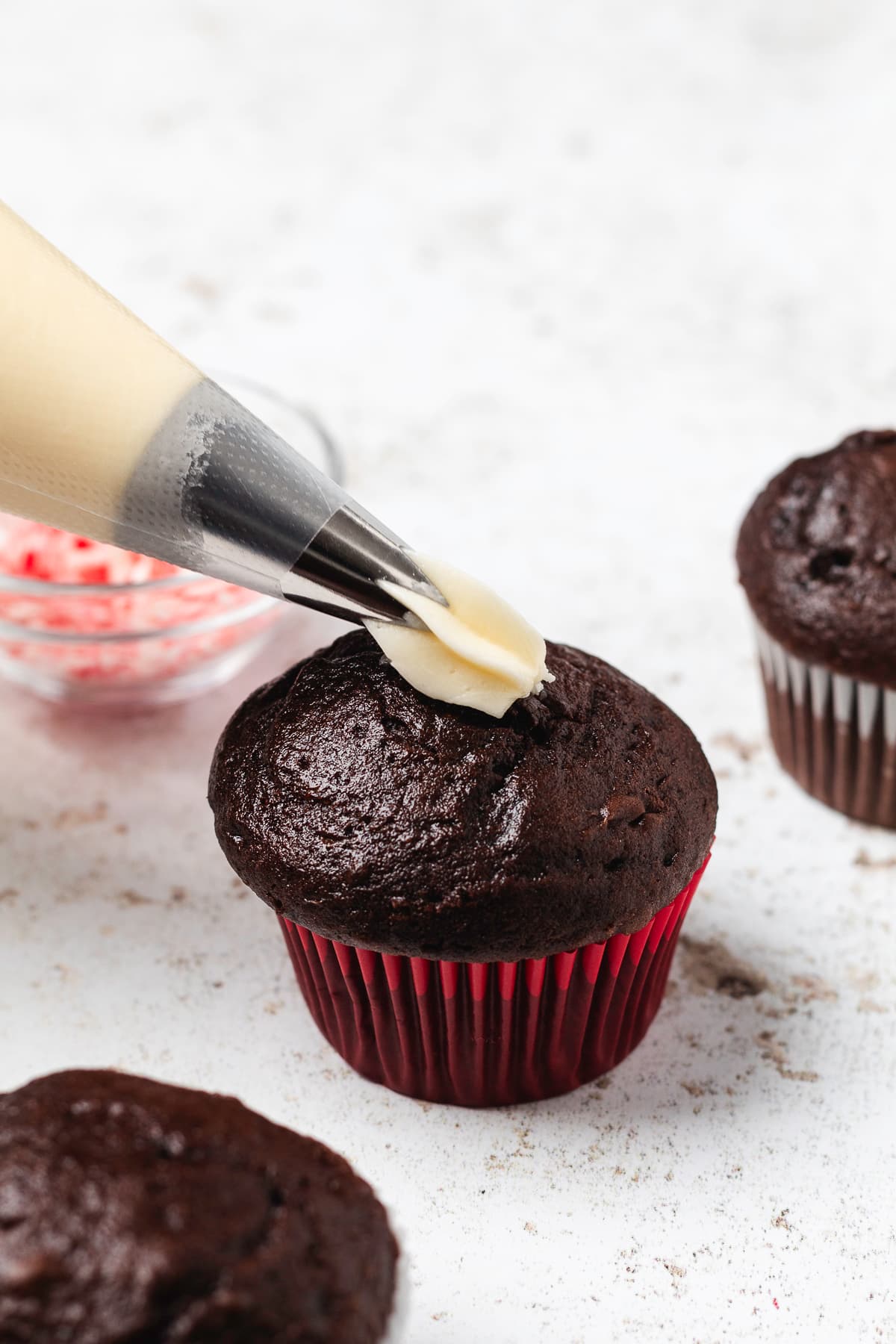 Creamy peppermint frosting being piped onto a chocolate cupcake in a red liner.