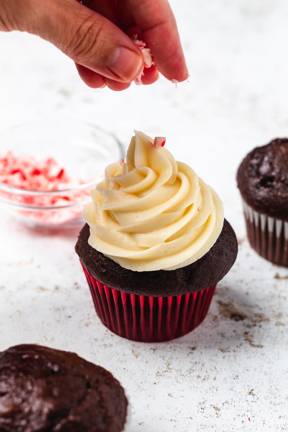 Crushed candy canes being sprinkled over a chocolate cupcake topped with swirled peppermint frosting.