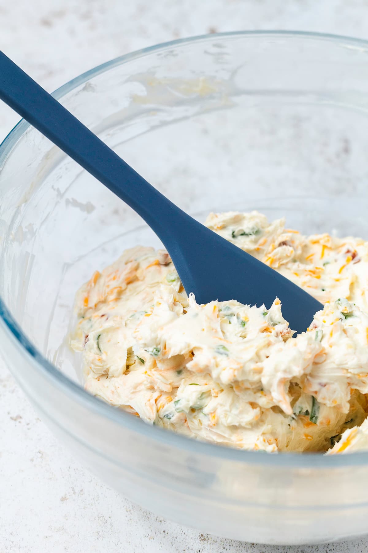 Creamy bacon jalapeño cheese ball mixture with shredded cheese and green onions in a glass bowl.