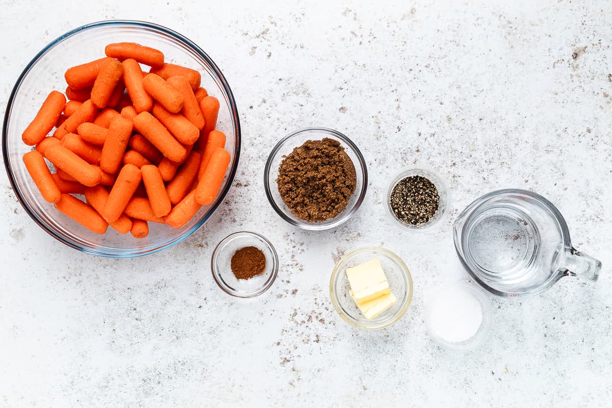 Overhead view of baby carrots, brown sugar, butter, cinnamon, salt, black pepper, and water for glazed carrots.