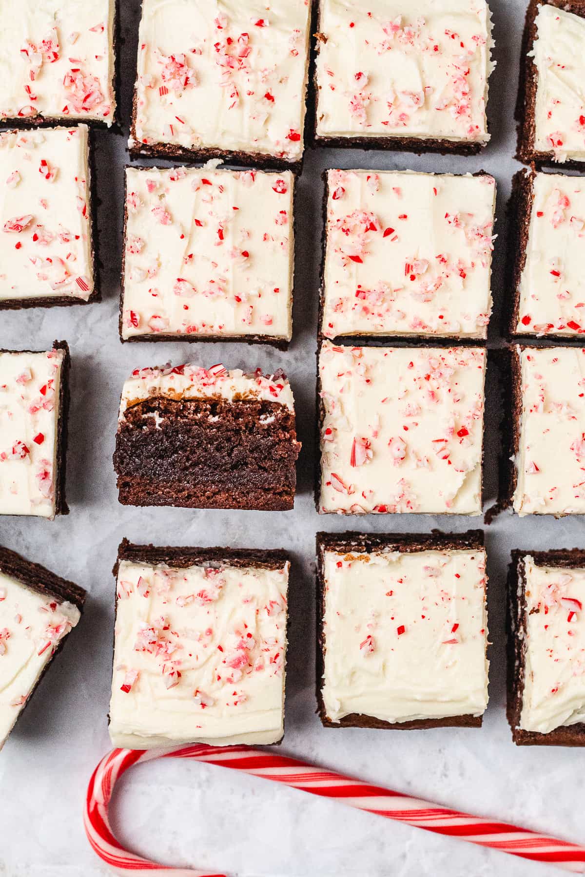 Fudgy chocolate brownies topped with peppermint frosting and crushed candy canes, arranged beside a candy cane.