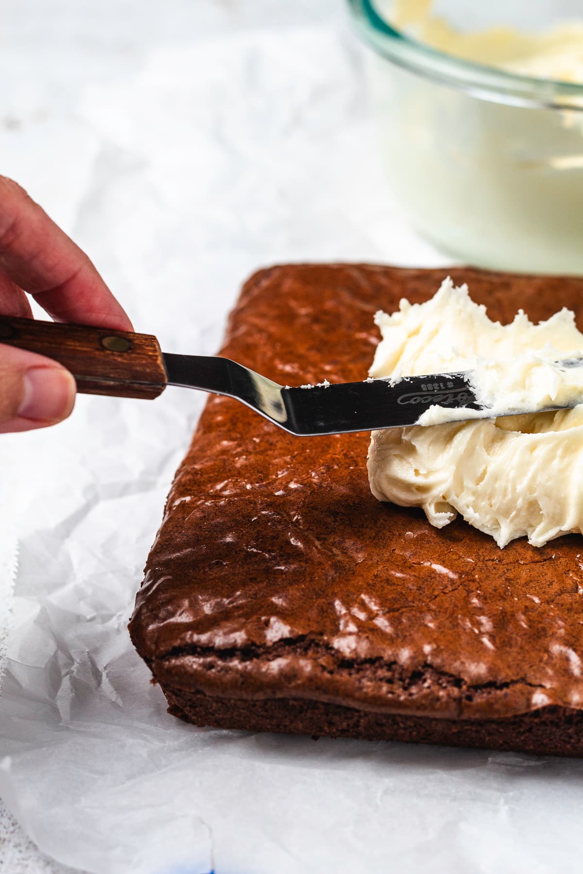 Thick, creamy peppermint frosting being spread over a pan of freshly baked chocolate brownies.