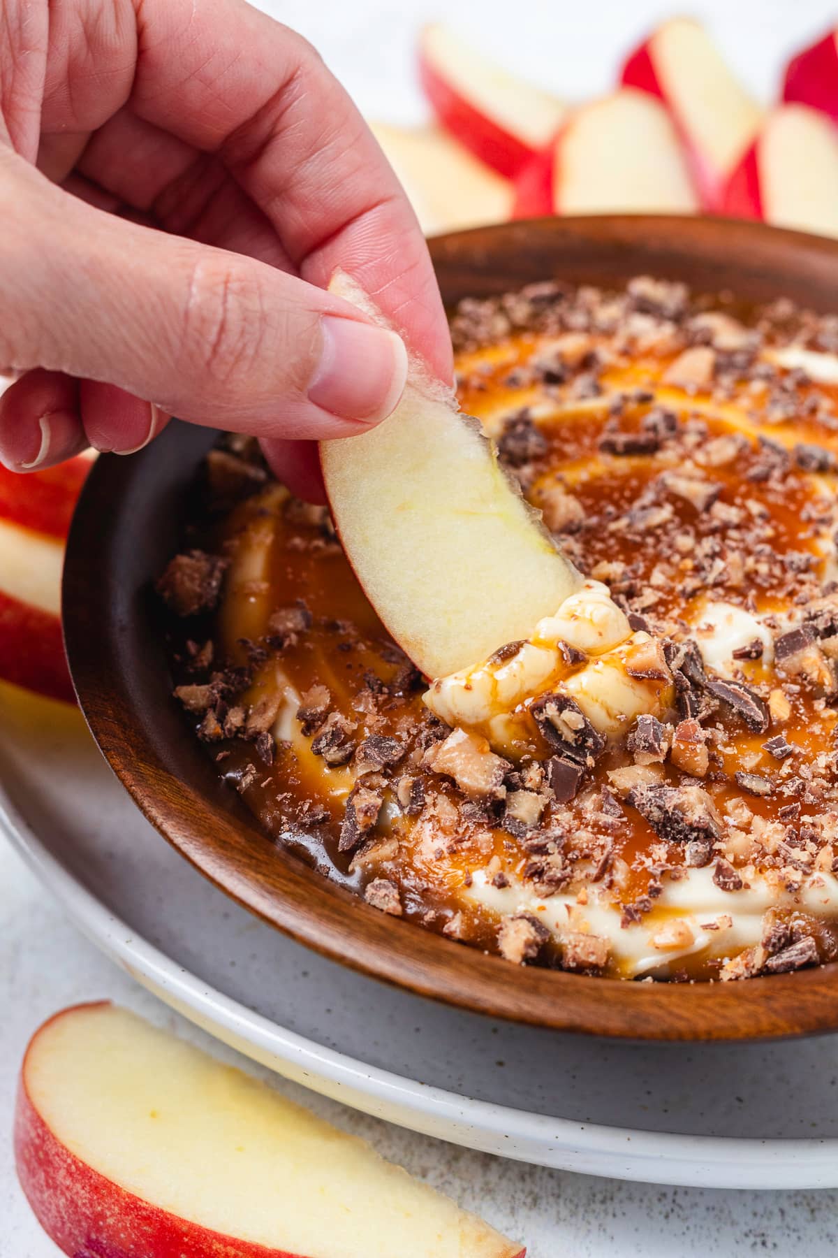 Dipping a fresh red apple slice into creamy caramel apple dip topped with chopped Heath bars.
