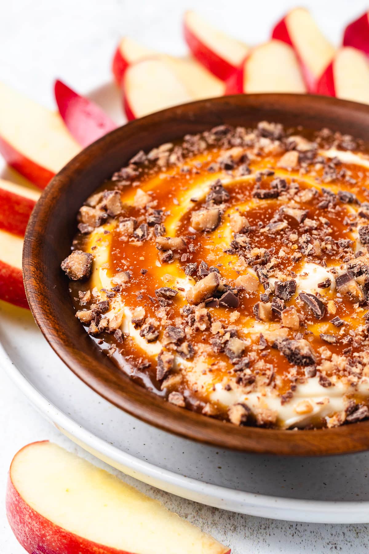 Creamy caramel apple cheesecake dip topped with chopped Heath bars and served with fresh red apple slices.
