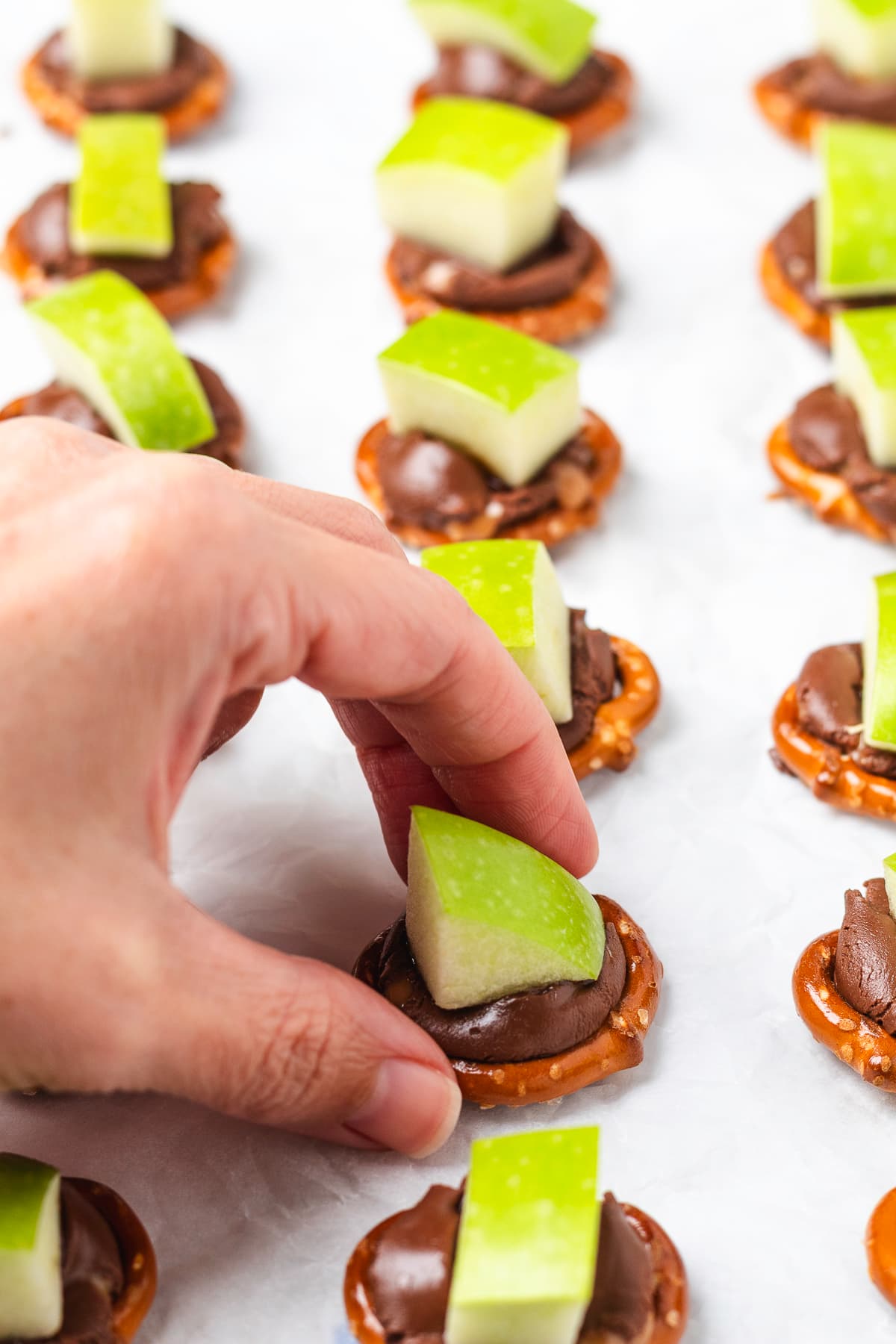 A hand picks up a caramel apple pretzel bite topped with a fresh green apple piece.
