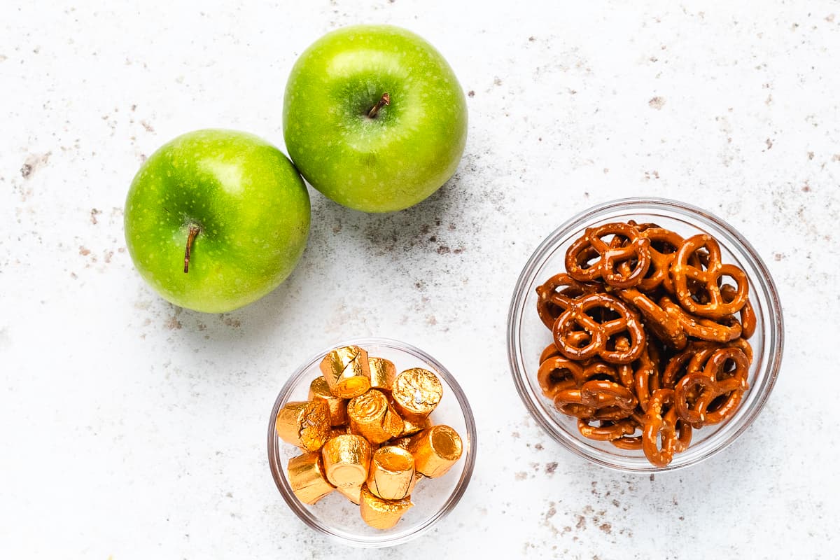 Green apples, Rolo candies, and mini pretzels arranged on a white countertop.