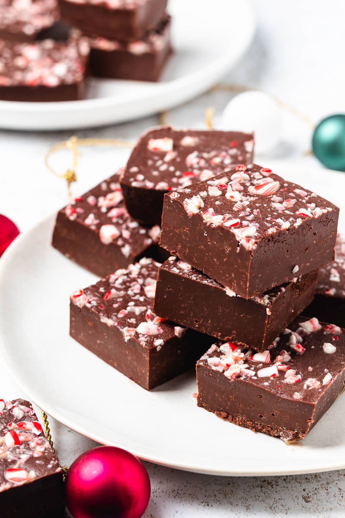 Rich chocolate peppermint fudge squares topped with crushed candy canes and stacked on a white plate.