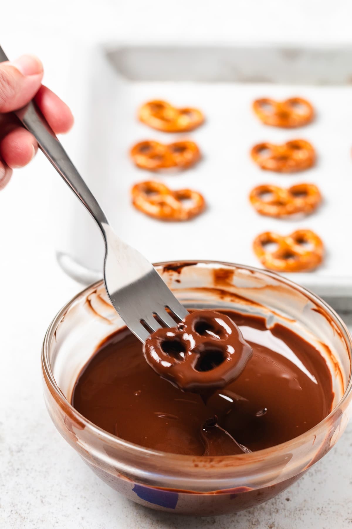 Mini pretzel coated in melted chocolate being lifted from a glass bowl with a fork