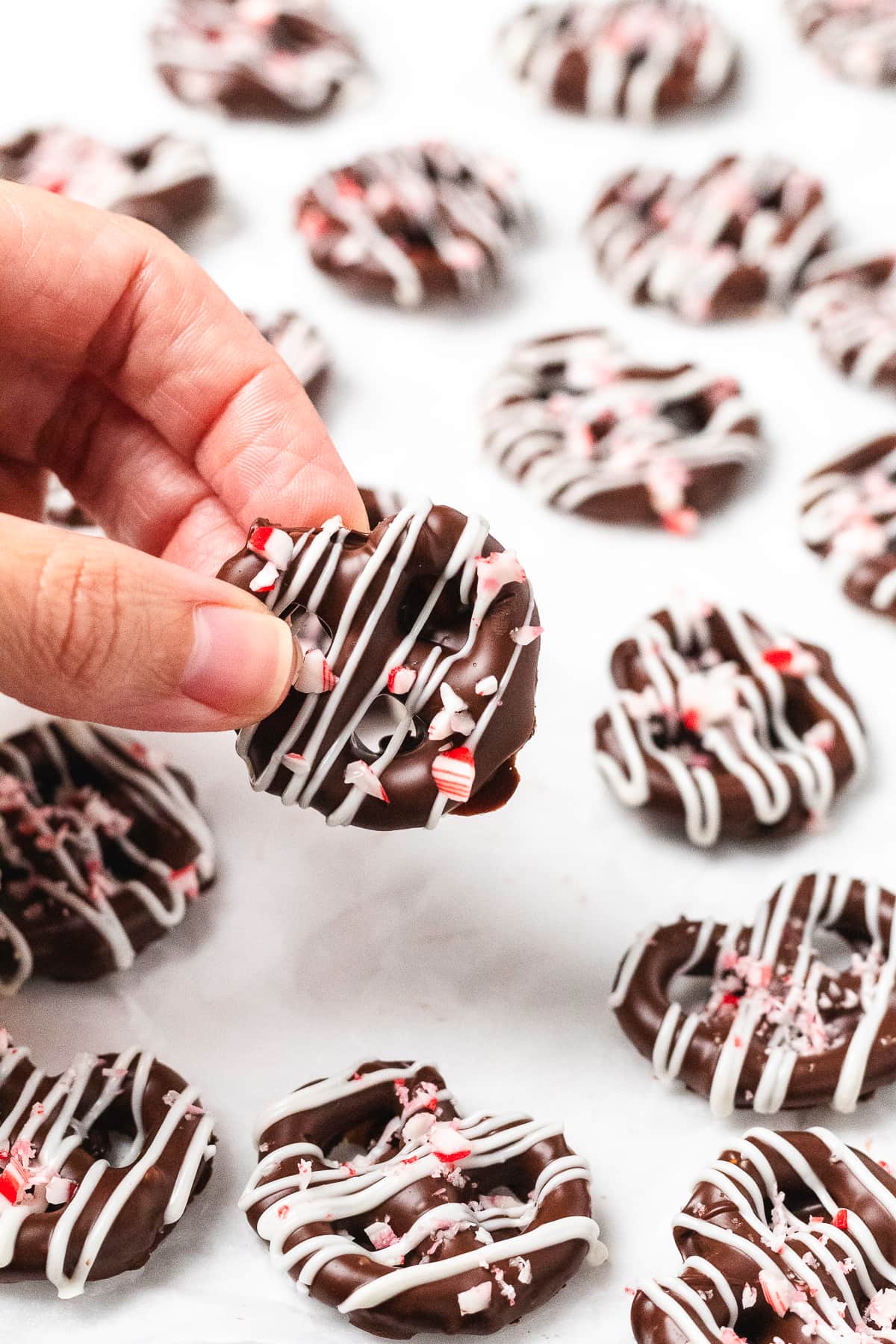 Hand holding a chocolate peppermint pretzel with white chocolate drizzle and crushed candy canes.
