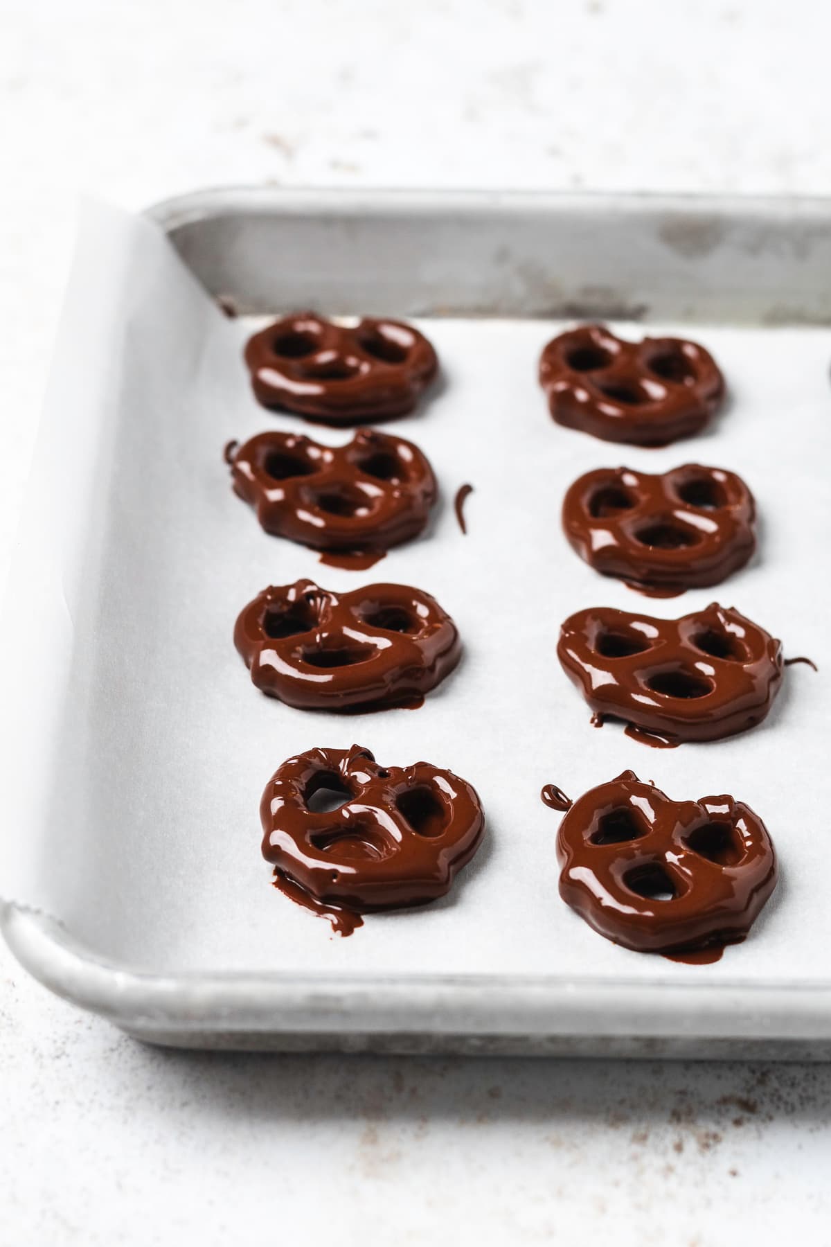 Freshly dipped chocolate pretzels arranged on a parchment-lined baking sheet.