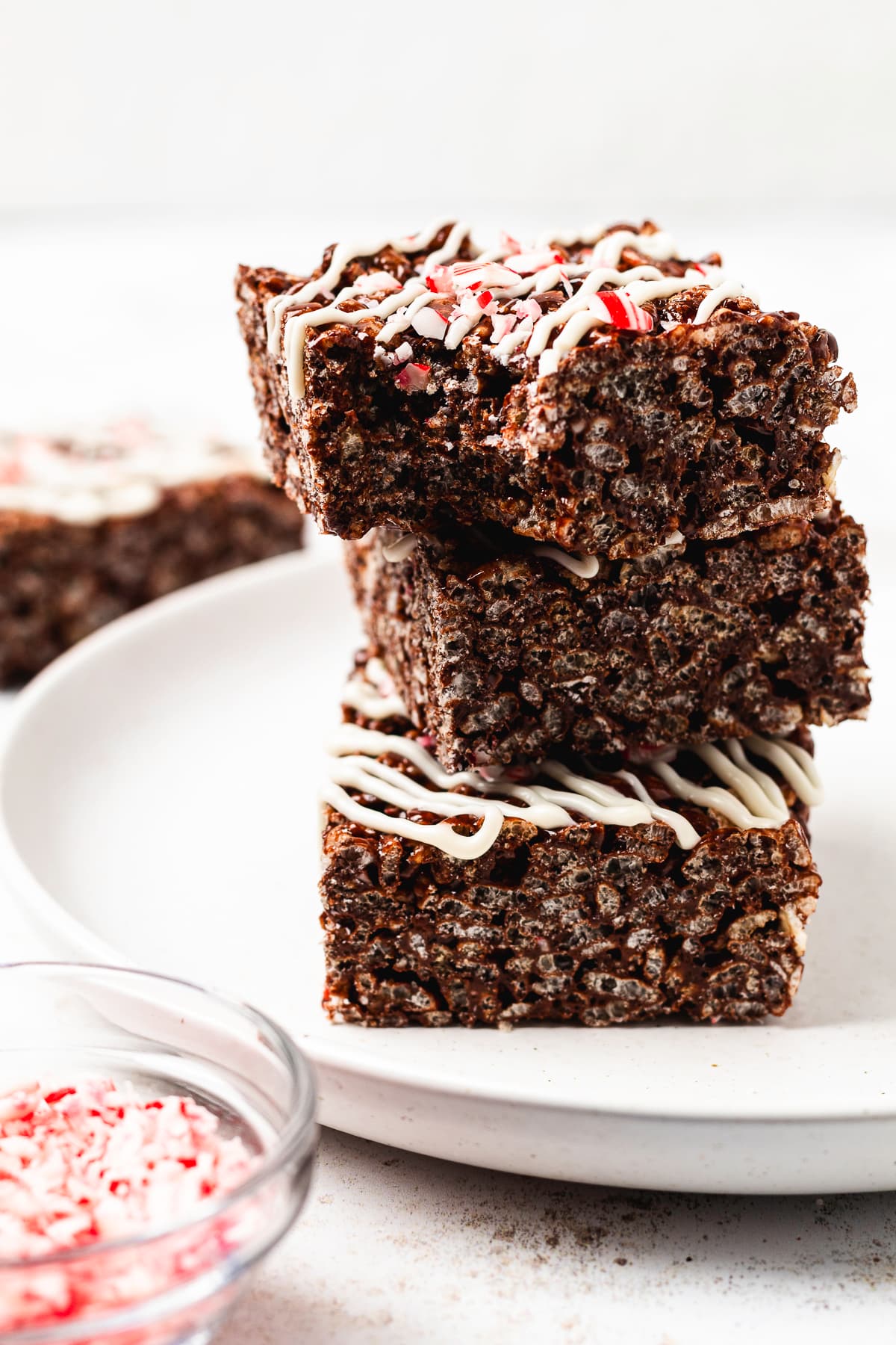 Three thick chocolate peppermint Rice Krispie treats stacked with white chocolate drizzle and crushed candy canes.