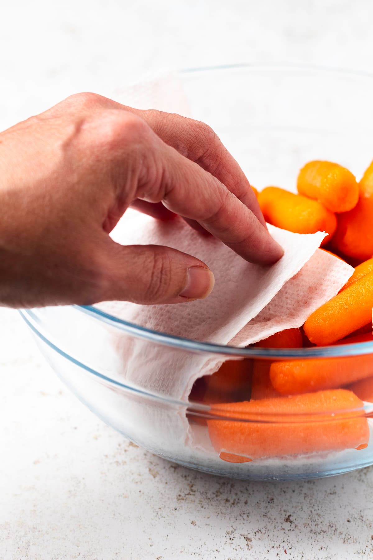 Patting baby carrots dry with a paper towel in a glass bowl before adding the honey glaze.