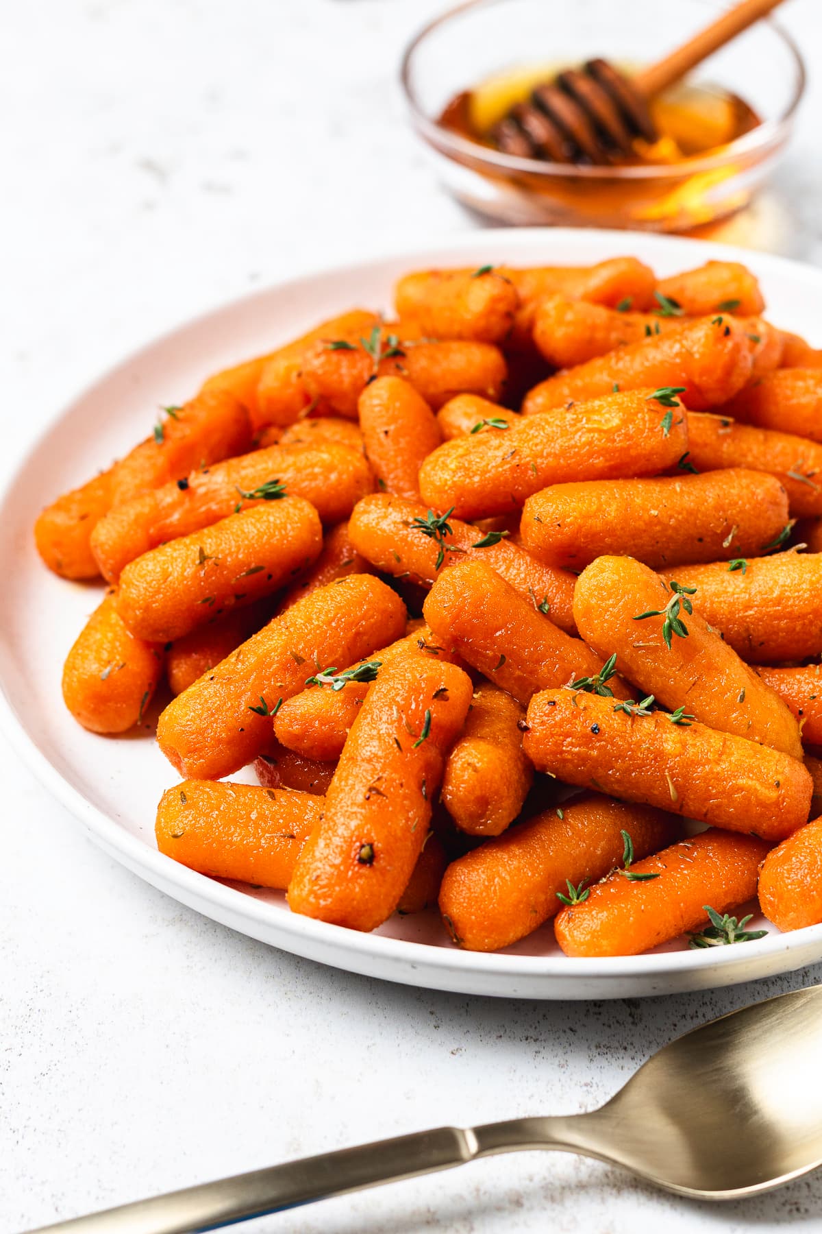 Honey roasted baby carrots coated in a glossy glaze and garnished with fresh thyme on a white plate.