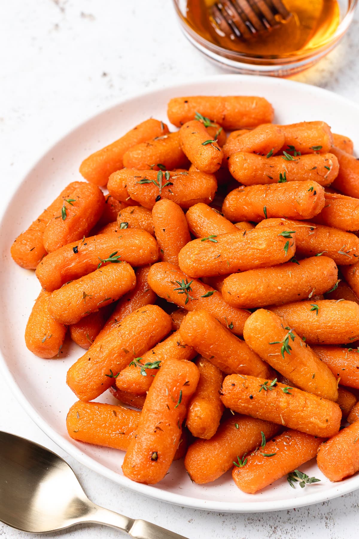 Close-up of honey glazed roasted baby carrots sprinkled with fresh thyme on a white serving plate.