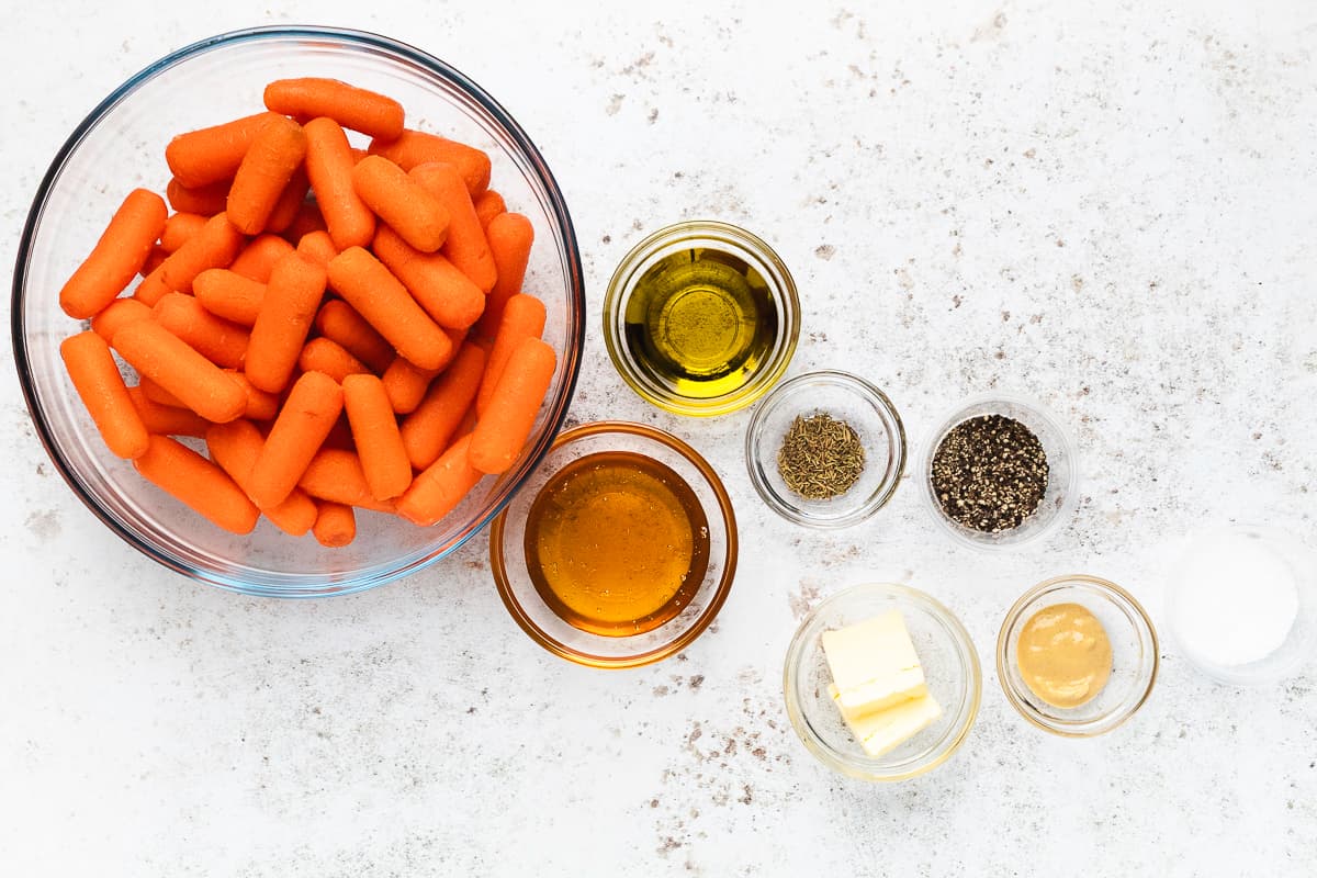 Overhead view of baby carrots, honey, olive oil, butter, mustard, and seasonings for honey roasted carrots.