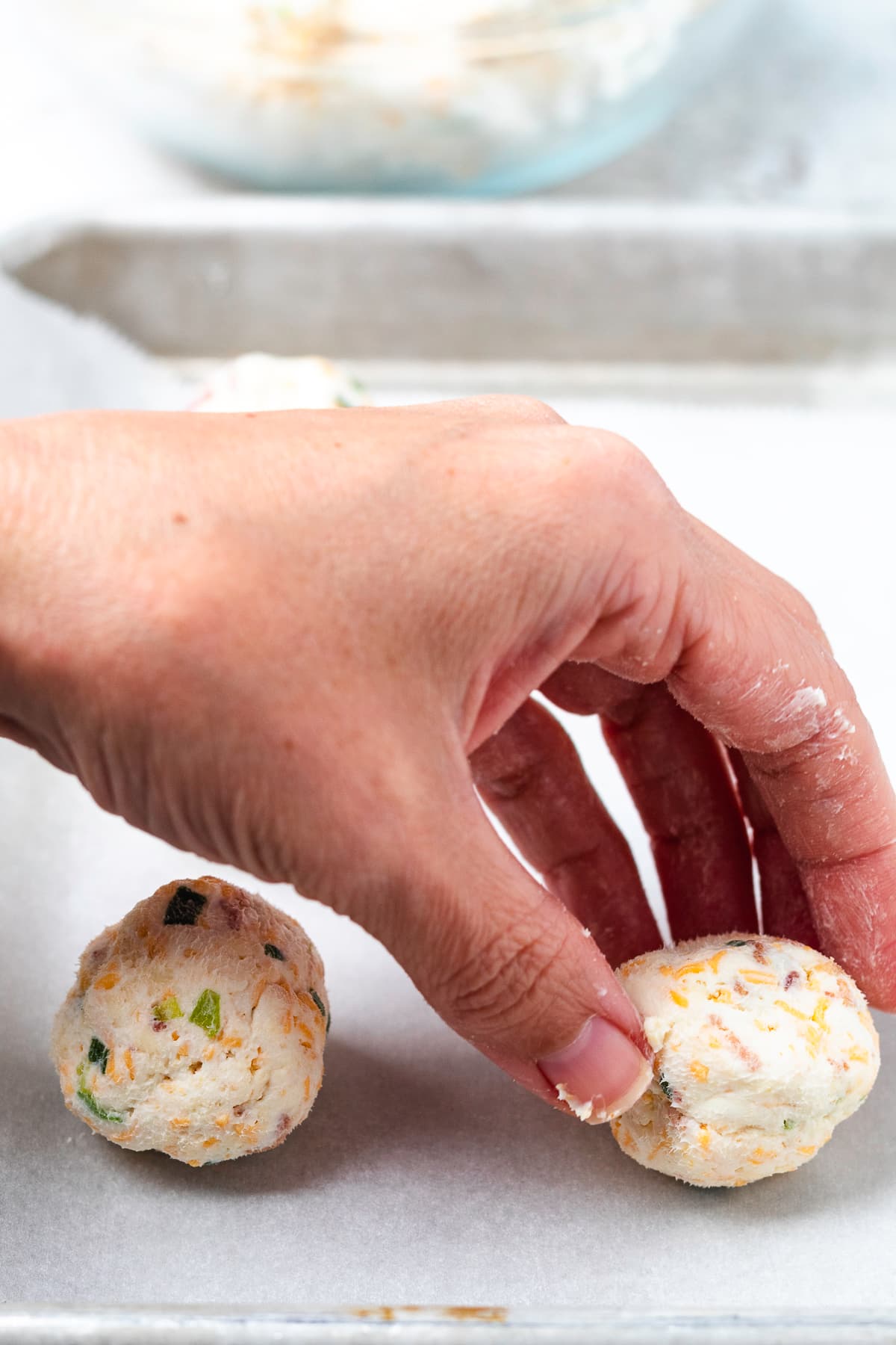 A hand shapes individual mini cheese balls on a parchment-lined baking sheet.
