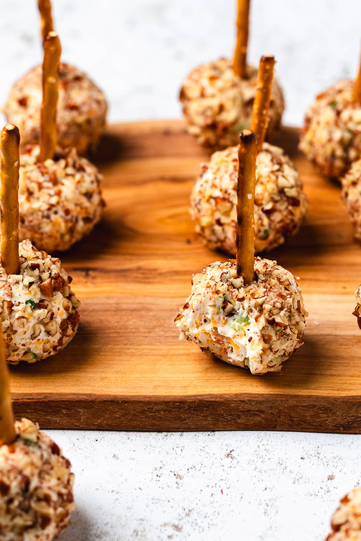Mini cheese balls coated in chopped pecans and served with pretzel stick handles on a wooden board.