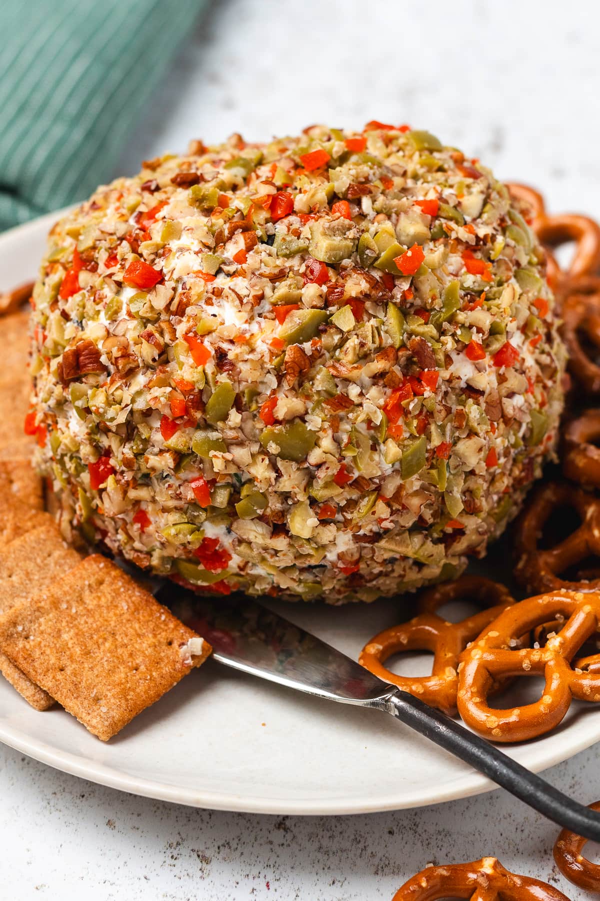 Olive cheese ball coated with chopped olives, pecans, and peppers, served with crackers and pretzels.