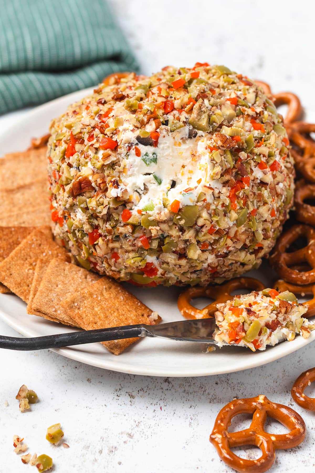 Olive cheese ball with a creamy center exposed, served with crackers, pretzels, and a cheese spreader.