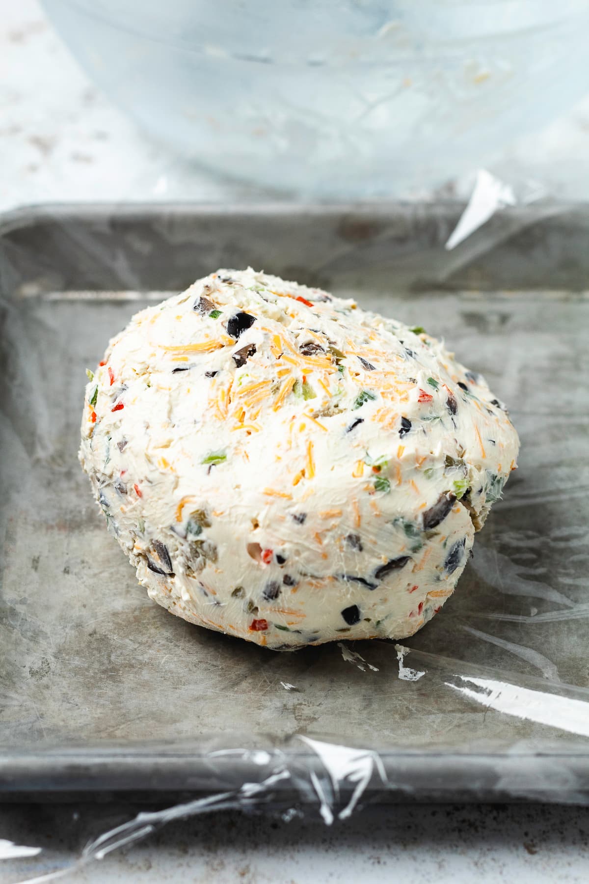 Homemade olive cheese ball on plastic wrap, ready to be wrapped and chilled.