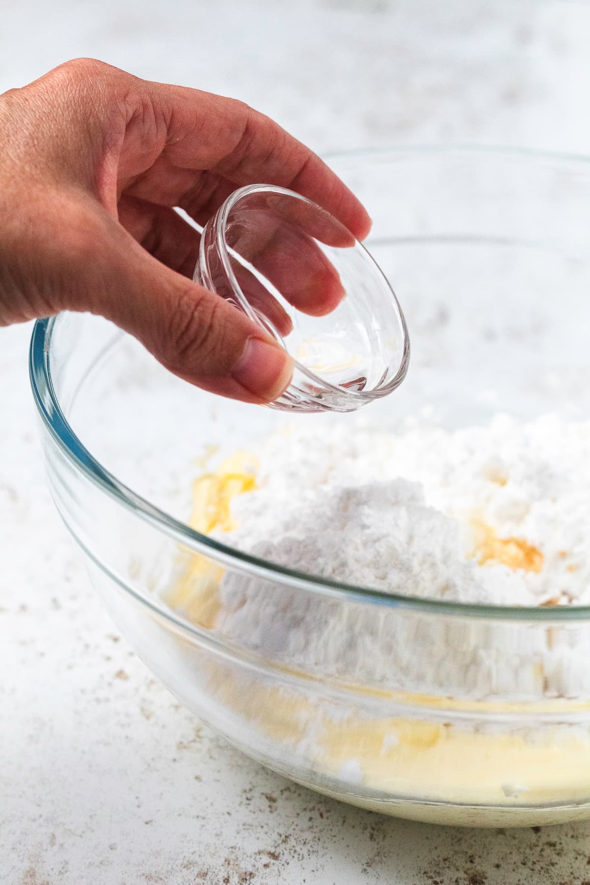 Peppermint extract being poured into a mixing bowl with butter and powdered sugar.