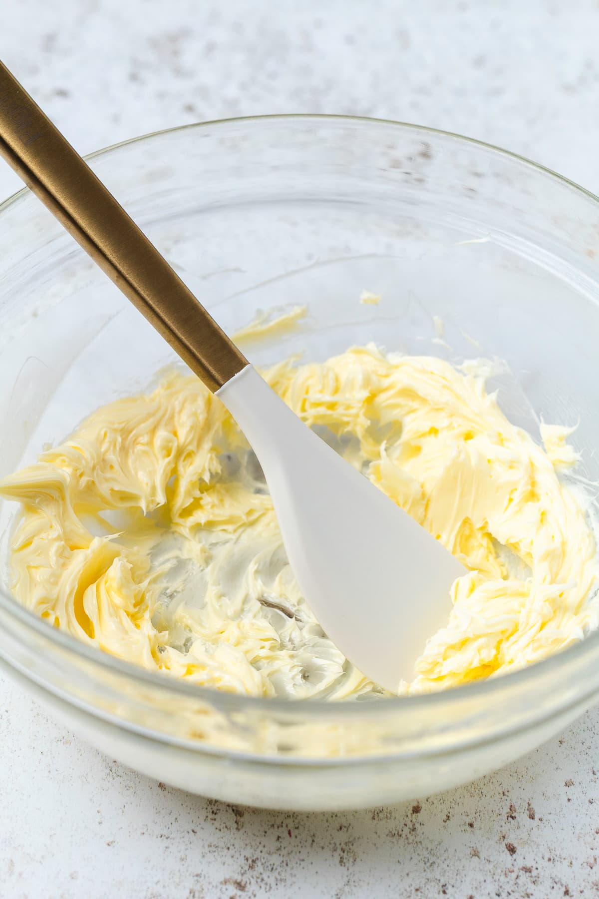 Soft, creamy butter in a glass mixing bowl with a spatula.