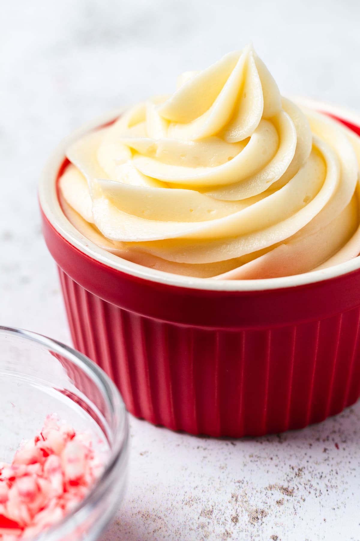 Creamy peppermint buttercream frosting piped into a red bowl beside crushed candy canes.