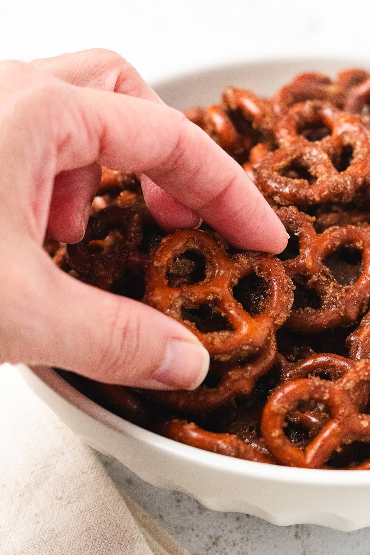 A hand picking up a pumpkin spice pretzel from a bowl of sweet, crunchy seasoned pretzels.